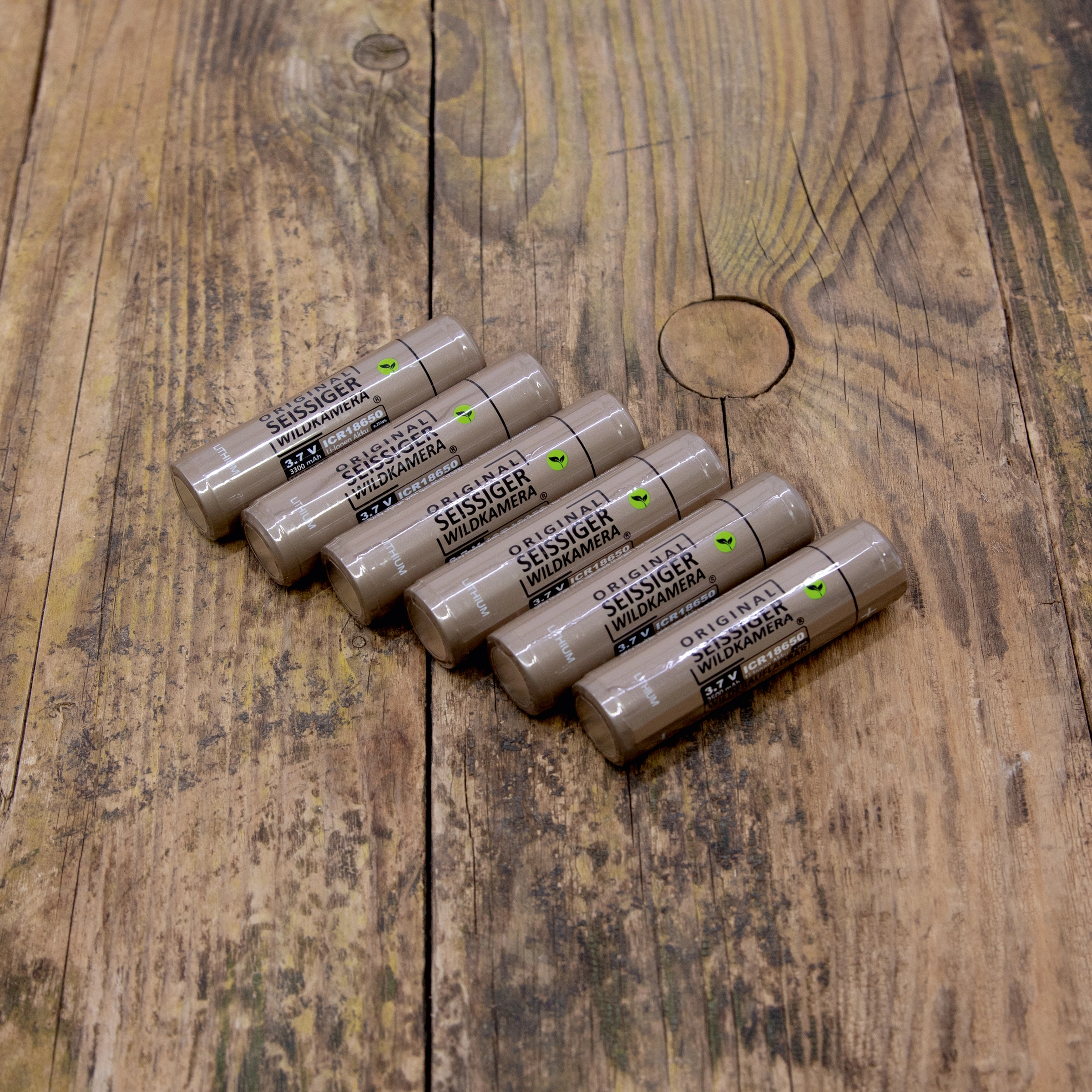 Sechs zylindrische Seissiger 18650 Li-Ion-Akkus mit Aufschrift 'ORIGINAL SEISSIGER WILDKAMERA' liegen nebeneinander auf einer Holzoberfläche